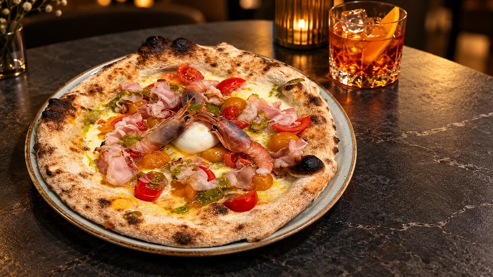 La pizza Genesi al centro del tavolo, con un drink accanto